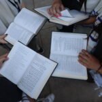 Jewish Youth Climate Movement teens holding siddurim (prayer books) and wearing tallit (prayer shawls) while standing in a circle.