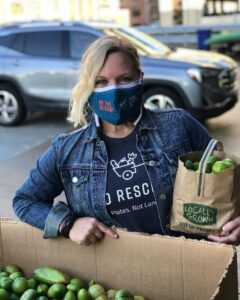Woman wearing a mask holding a bag of fresh green tomatoes.